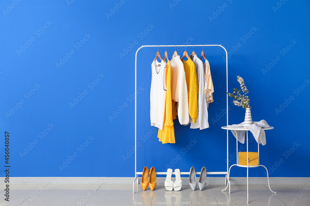 Rack with stylish clothes and table near color wall