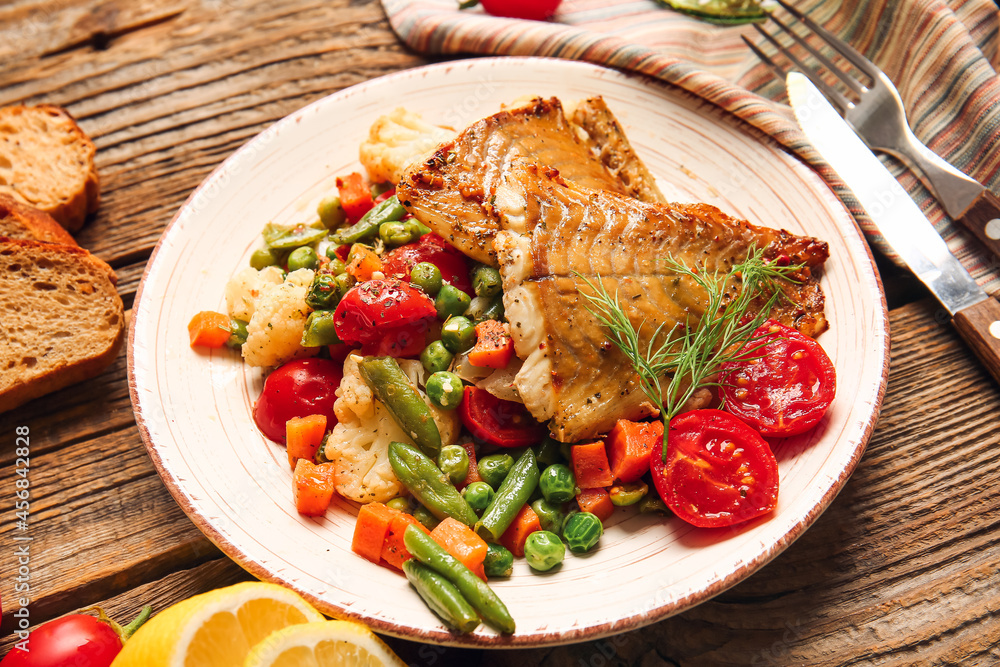 Plate with tasty baked cod fillet and vegetables on wooden background, closeup