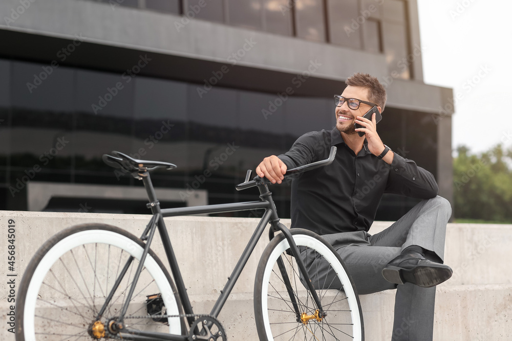 Businessman with bicycle talking by mobile phone on city street