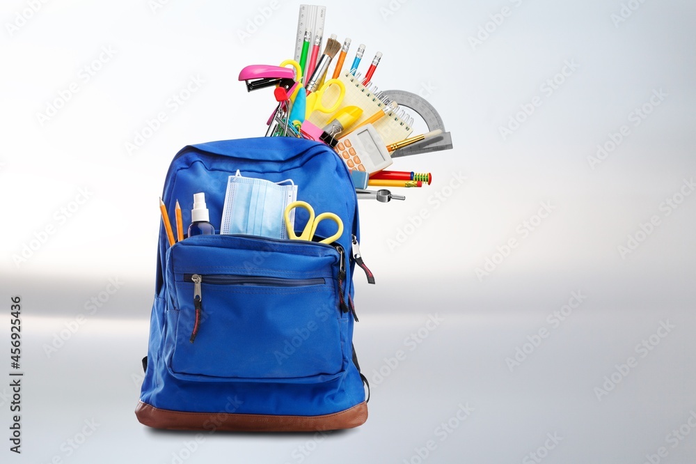 School backpack with colored set of stationery on background