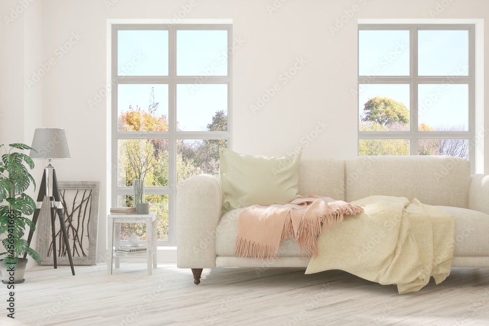 Stylish room in white color with sofa and autumn landscape in window. Scandinavian interior design. 