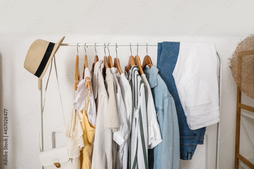 Rack with stylish clothes near light wall