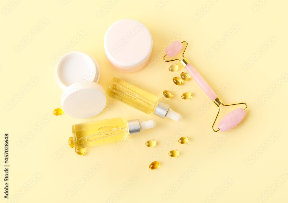 Cosmetic products with pills and facial massage tool on color background