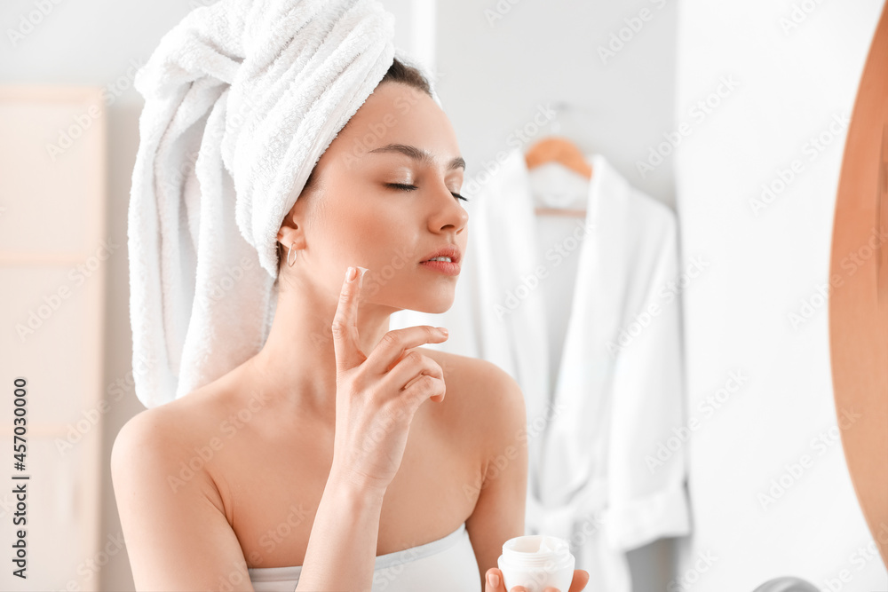 Young woman applying facial cream in bathroom