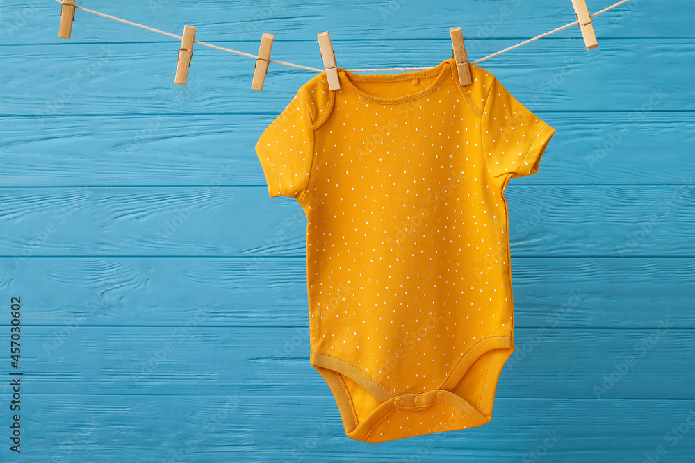 Baby clothes hanging on rope against color wooden background