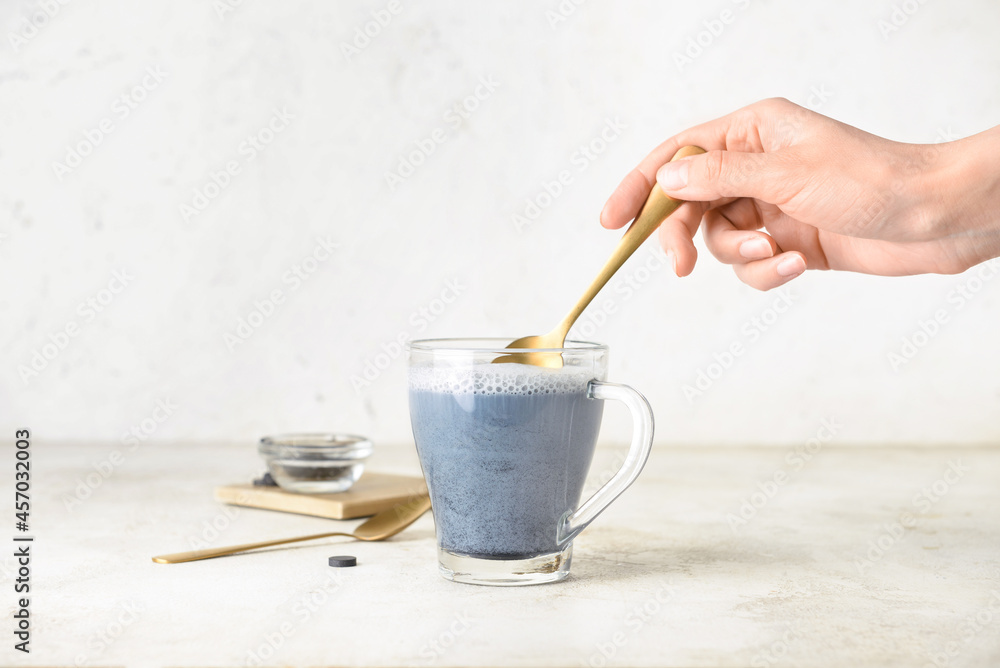 女人在浅色背景下用玻璃杯搅拌美味的木炭拿铁