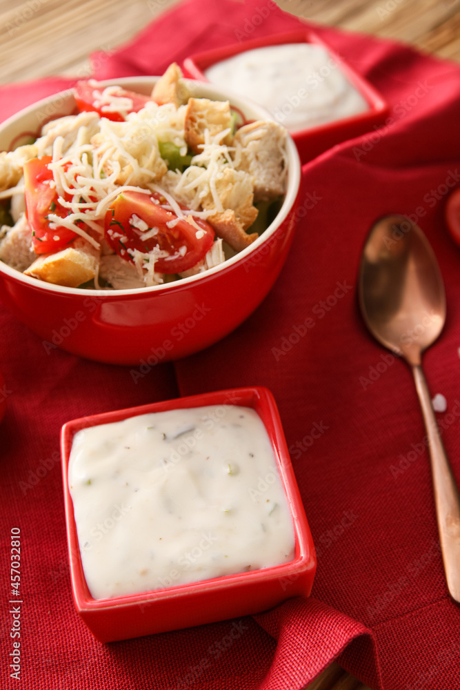 Bowl of tasty Caesar salad and sauce on table