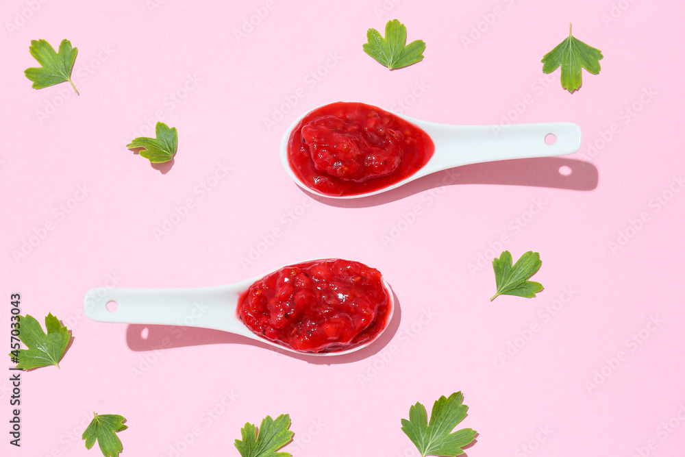 Spoons with tasty red currant jam and leaves on color background