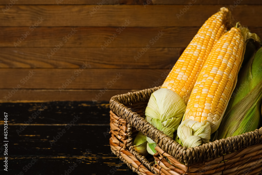 Wicker basket with fresh corn cobs on dark wooden table