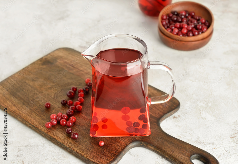 Jug of tasty tea with cranberry on light background