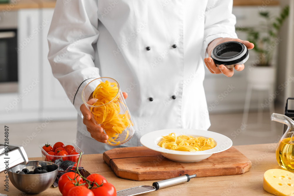 Male chef with tagliatelle pasta in kitchen, closeup