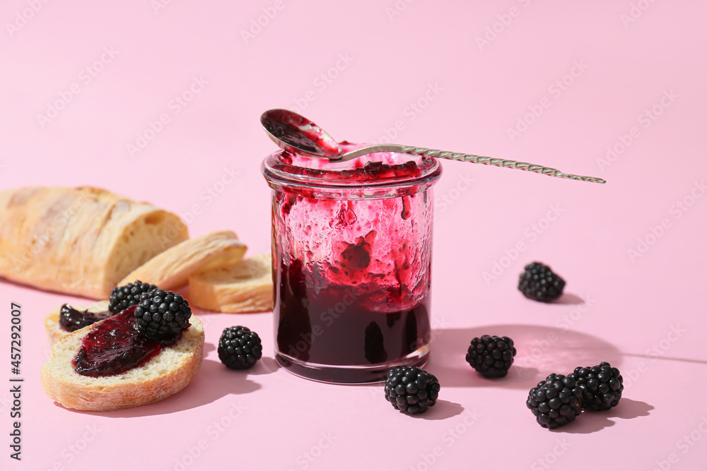 Jar of tasty blackberry jam and sandwiches on color background