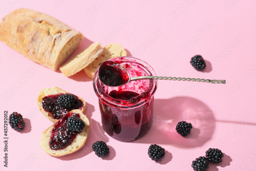 Jar of tasty blackberry jam and sandwiches on color background