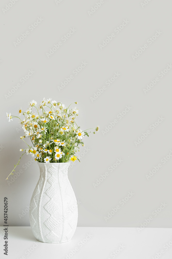 Vase with chamomiles on table near light wall