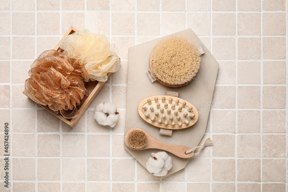 Different massage brushes and bath supplies on light tile background