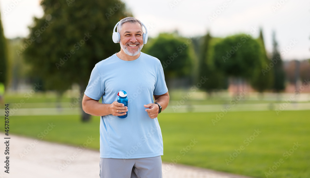 Happy positive mature man with broad smile holding water bottle while doing sport in city park