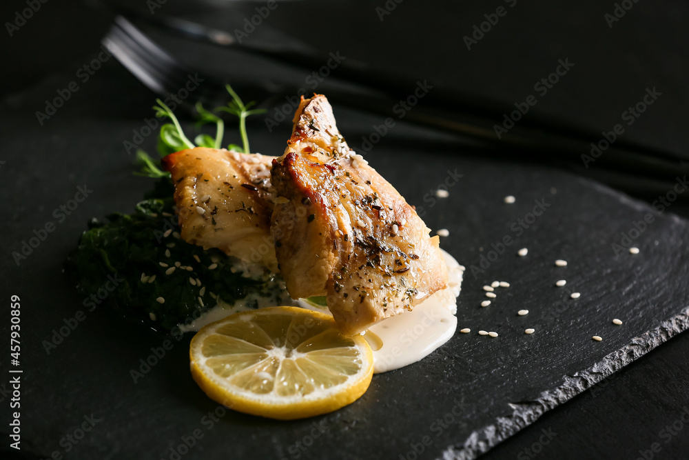 Board with baked cod fillet, pesto sauce and lemon on table in restaurant