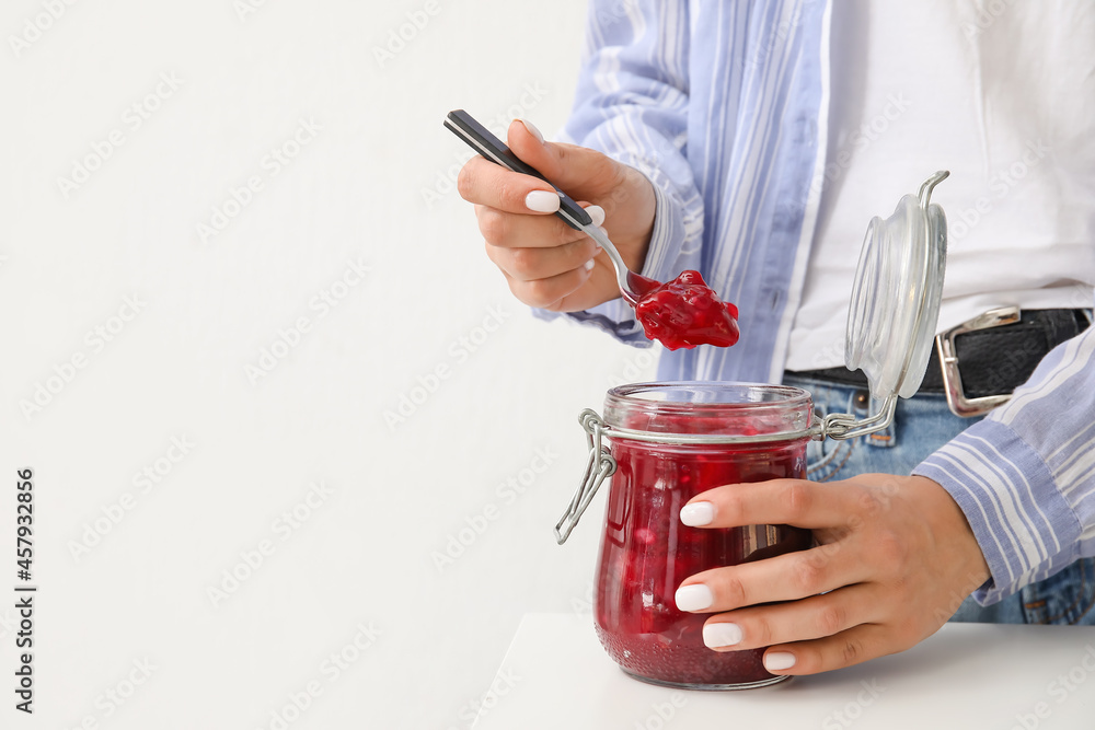 Woman with glass jar of cherry jam on light background, closeup