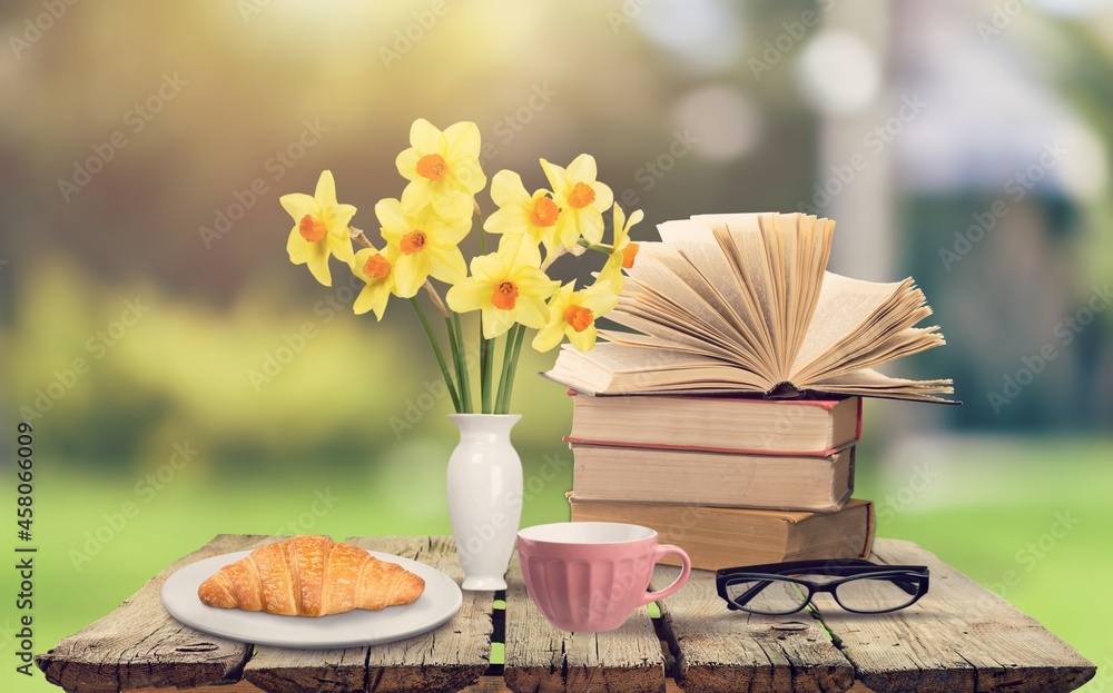 Bouquet of meadow flowers, croissant, cup of tea or coffee, books on the desk