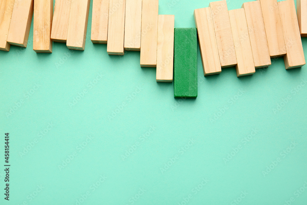 Green block among wooden ones on color background. Concept of uniqueness