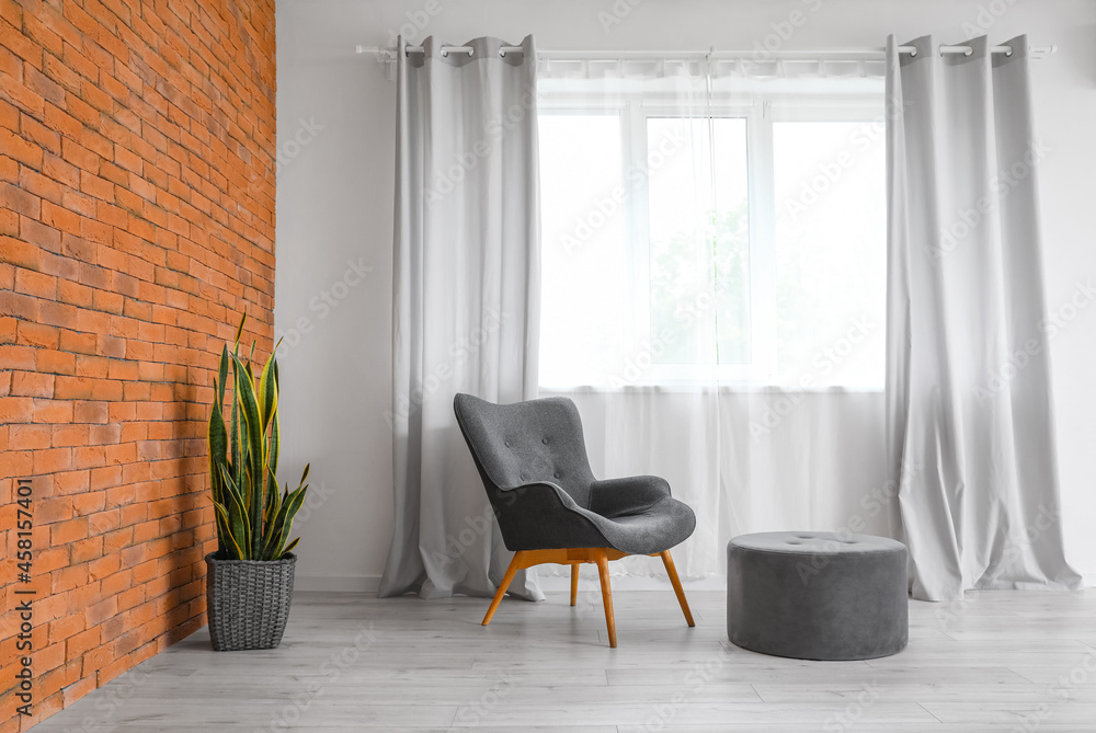 Modern armchair and pouf near window in room