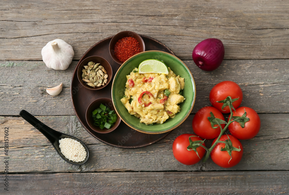 Bowl of tasty chicken curry and ingredients on wooden background