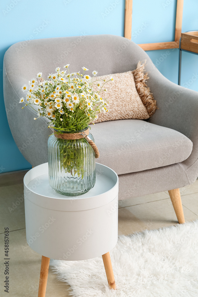 Vase with chamomiles on table in living room