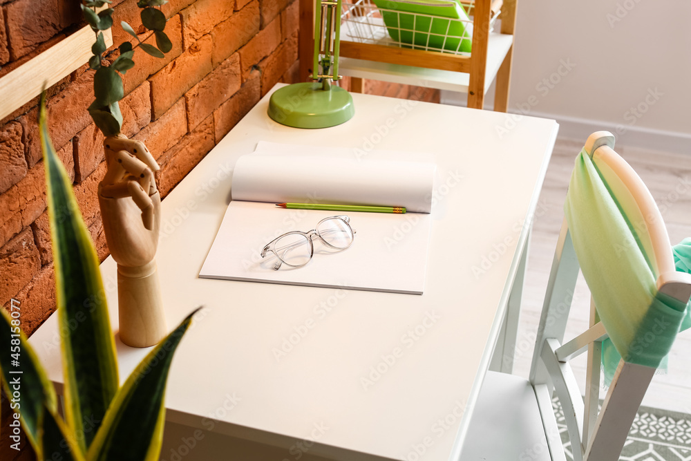 Comfortable workplace with notebook, pencil and eyeglasses on table near brick wall