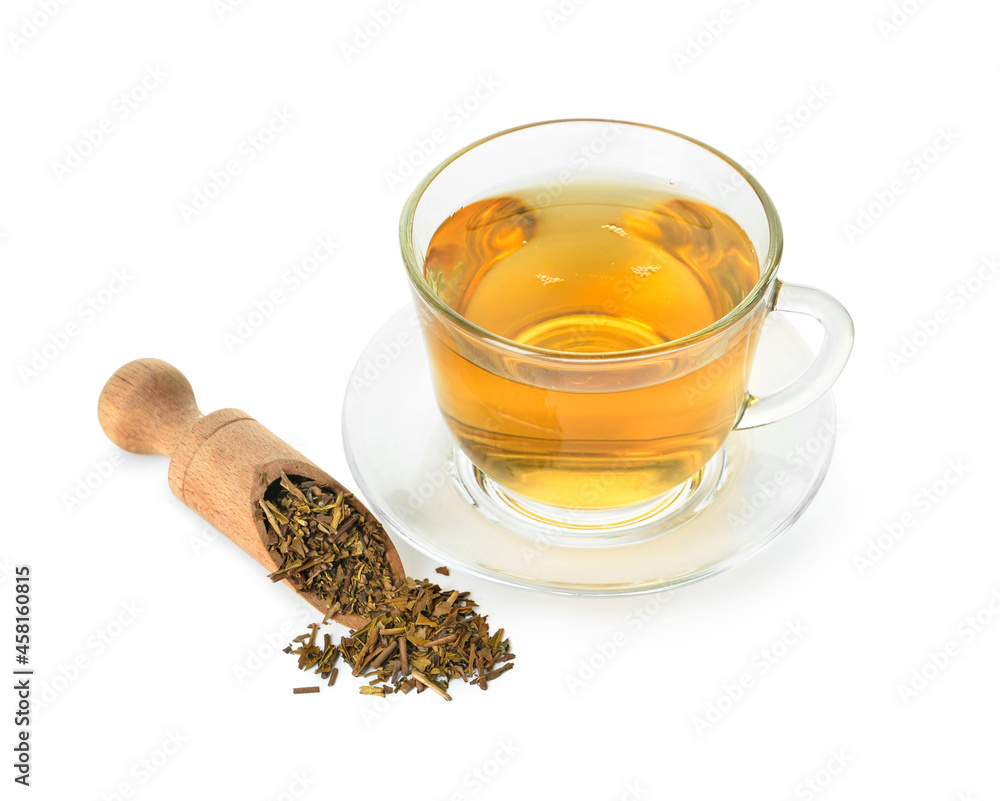 Scoop with dry hojicha green tea and cup of hot beverage on white background