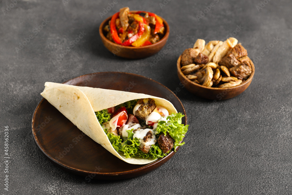 Plate with tasty Fajitas and ingredients on dark background