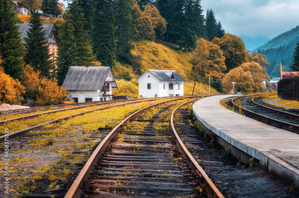 Railway station and small white house in mountain village in autumn in Europe. Rural railroad in fal