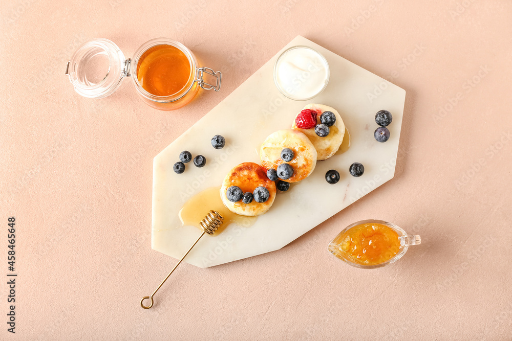 Board with tasty cottage cheese pancakes, berries and honey on color background