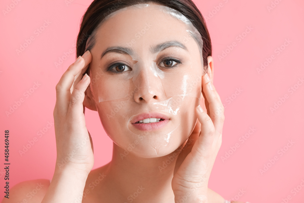 Beautiful young Asian woman with sheet facial mask on color background