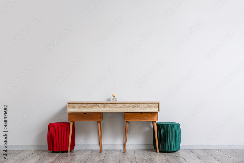 Wooden TV stand with reed diffuser and poufs near light wall