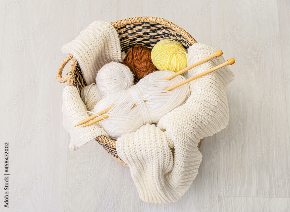 Basket with knitting yarn, needles and clothes on grey wooden background