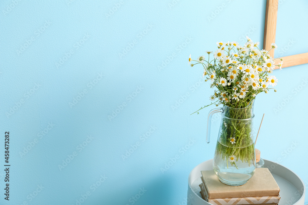 Vase with chamomiles and books on table near color wall