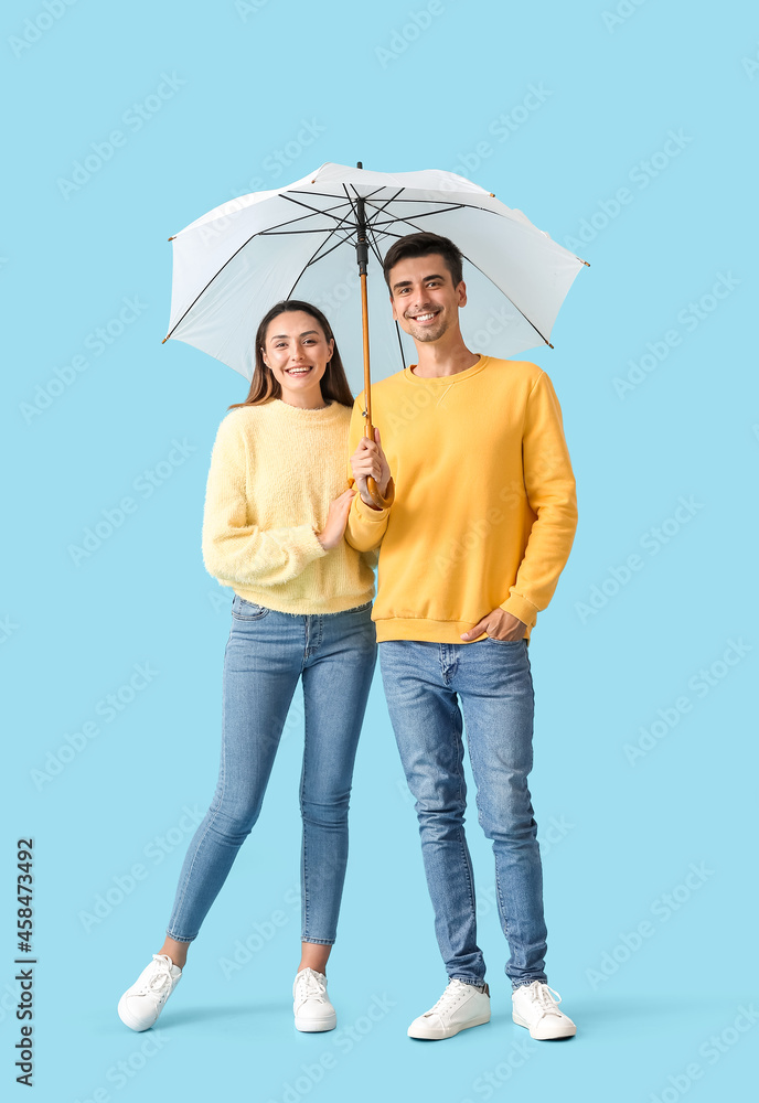 Young couple with umbrella on color background