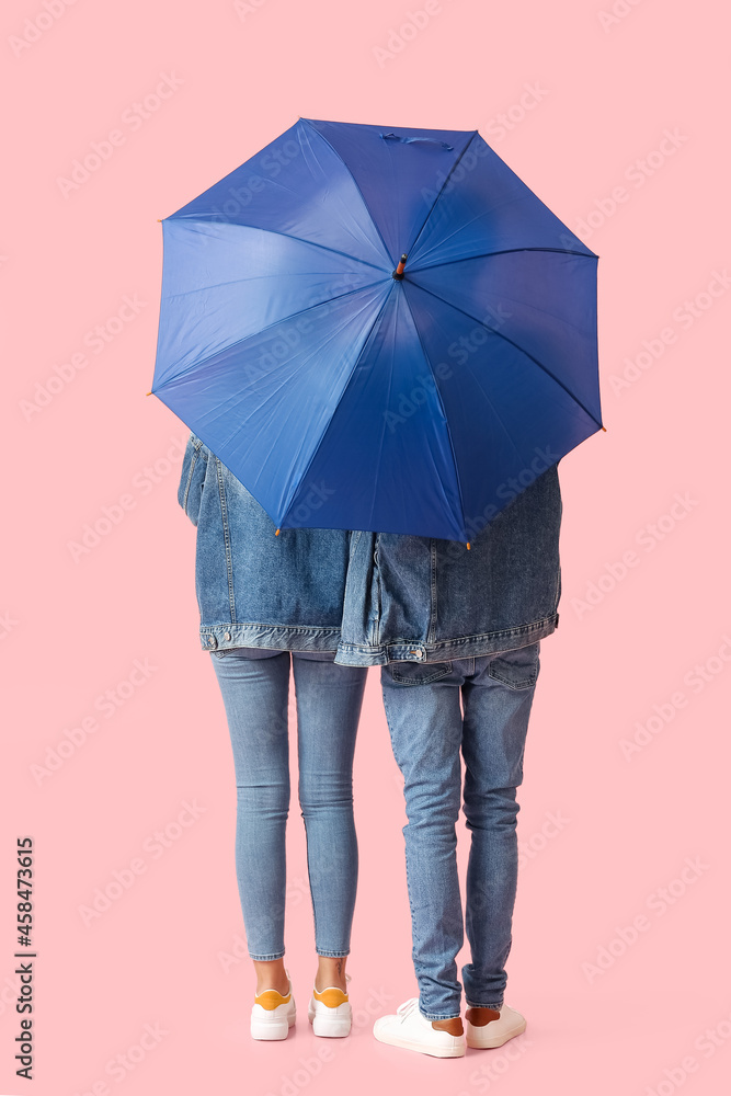 Young couple with umbrella on color background