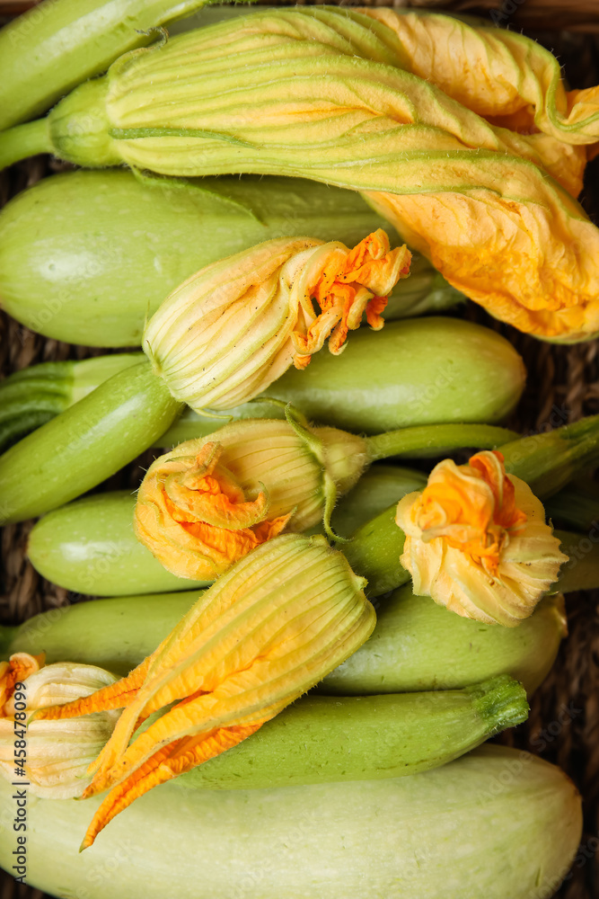 Fresh zucchini with flowers in wicker basket, closeup