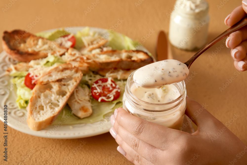 Woman with jar of tasty Caesar sauce on beige background