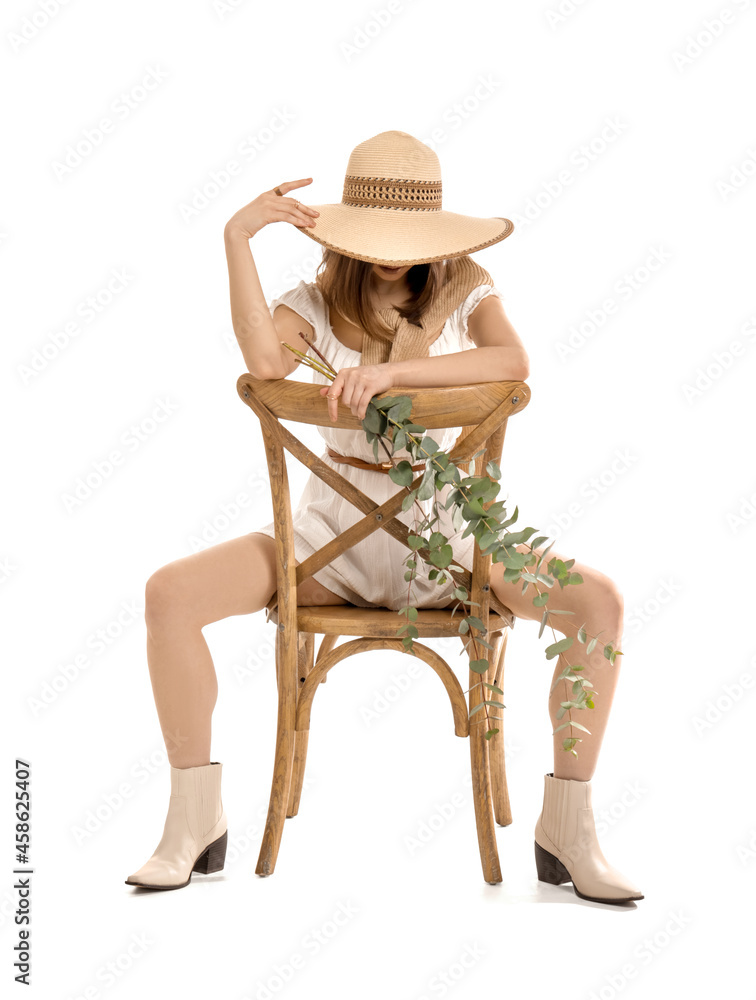 Beautiful young woman with eucalyptus branches sitting on chair against white background