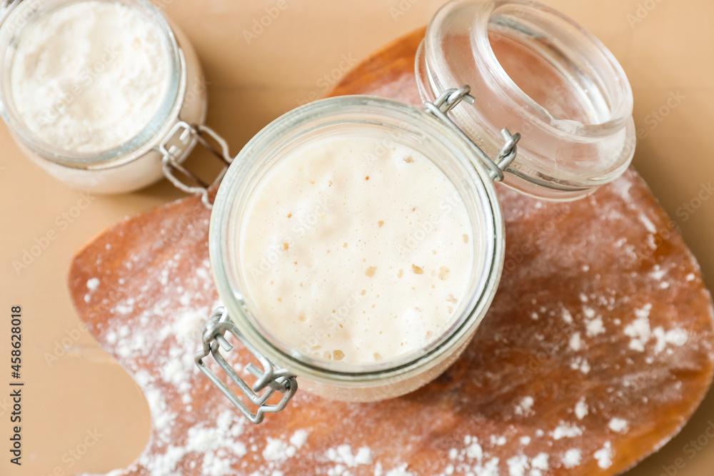 Glass jar with fresh sourdough on wooden background