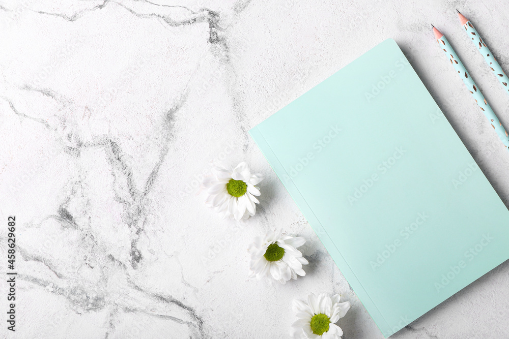 Notebook, pencils and chamomile flowers on light background