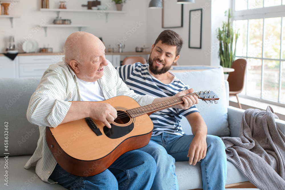 Senior man playing guitar for his son at home