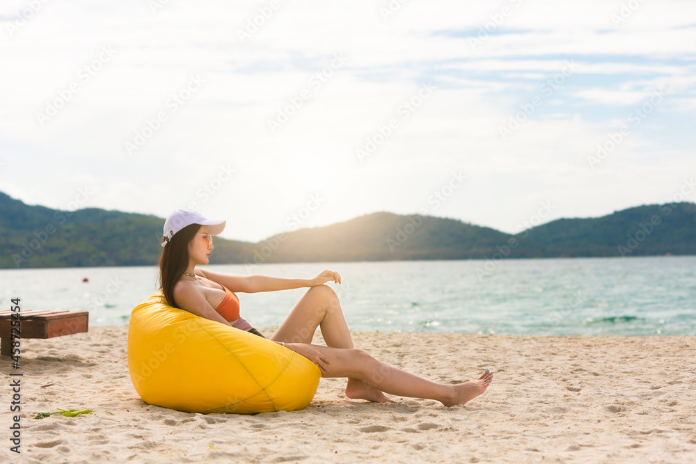 戴着帽子的亚洲女性在泰国的椅子海滩上放松身心。夏季海滩度假概念。