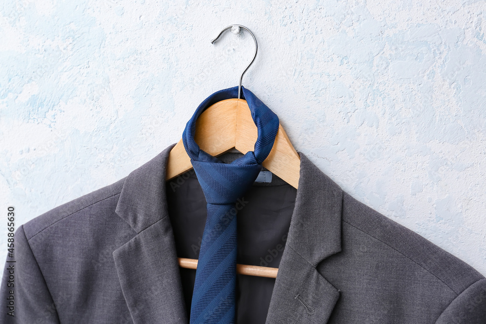 Hanger with stylish male suit hanging on white wall, closeup