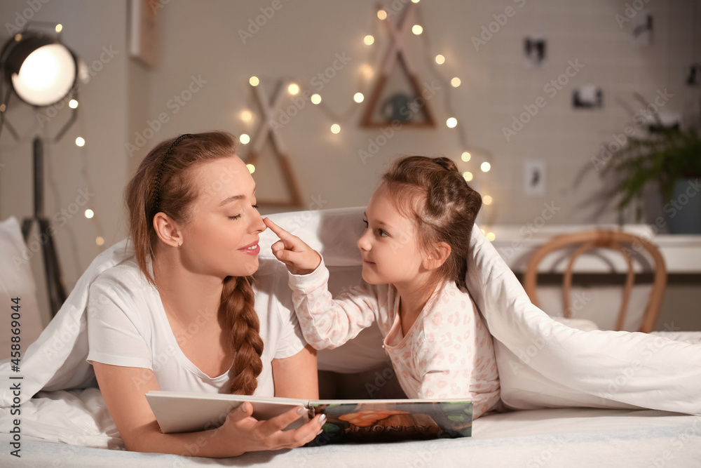 Little girl with her mother reading bedtime story before going to sleep