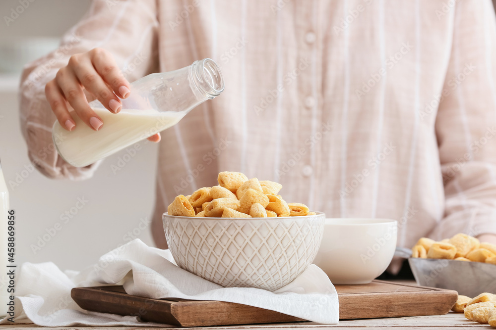 Woman pouring milk from bottle to bowl with delicious corn pillows on wooden table