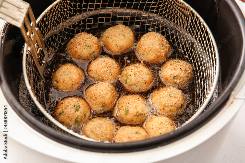 Cod cutlets preparing in deep fryer on table, closeup