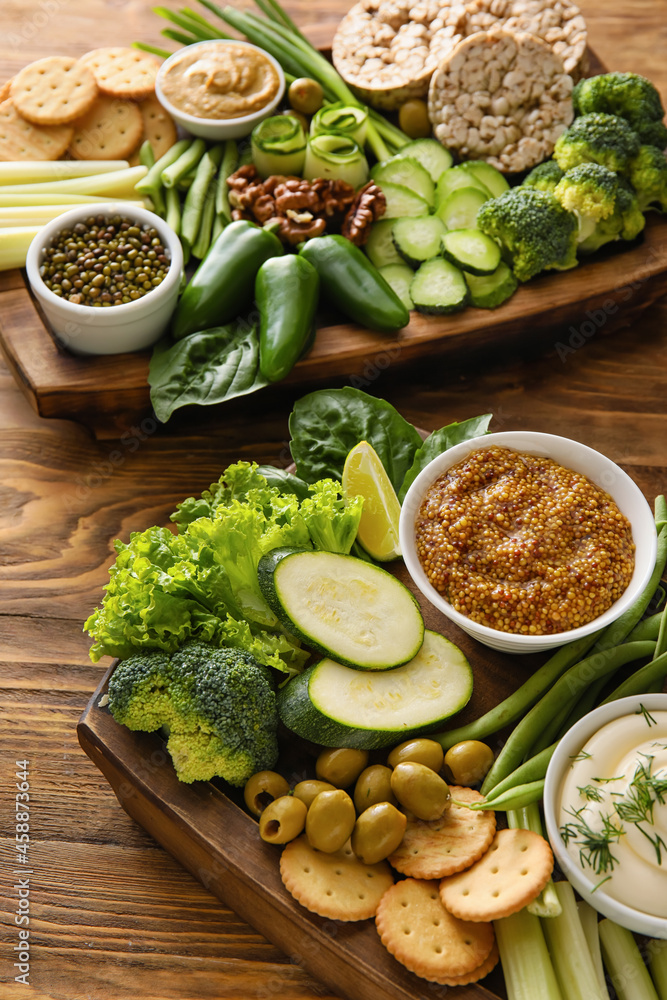 Boards with different green vegetables and bowls with sauce on wooden background, closeup